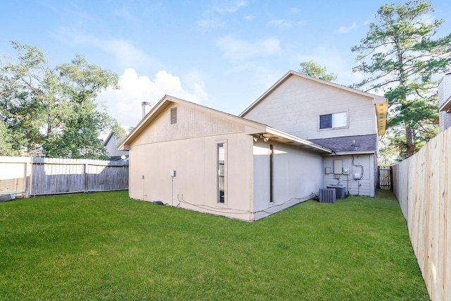 rear view of house with central AC unit and a lawn