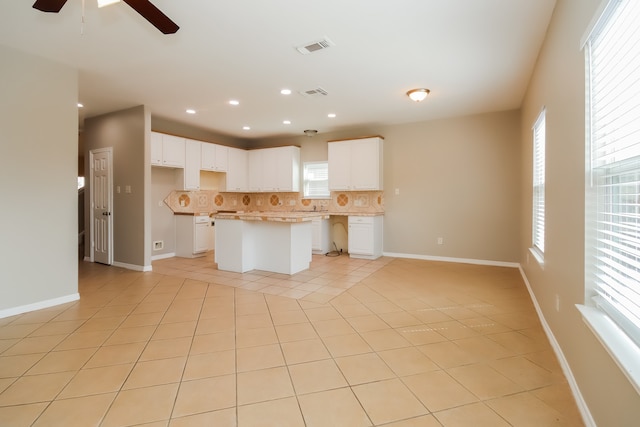 kitchen featuring light tile patterned floors, a center island, tasteful backsplash, and white cabinetry