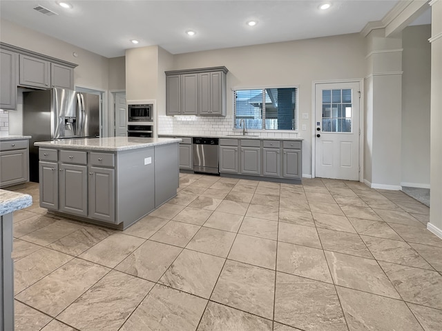 kitchen with tasteful backsplash, gray cabinetry, a kitchen island, and appliances with stainless steel finishes