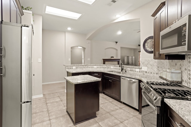 kitchen with sink, stainless steel appliances, light stone counters, backsplash, and a kitchen island