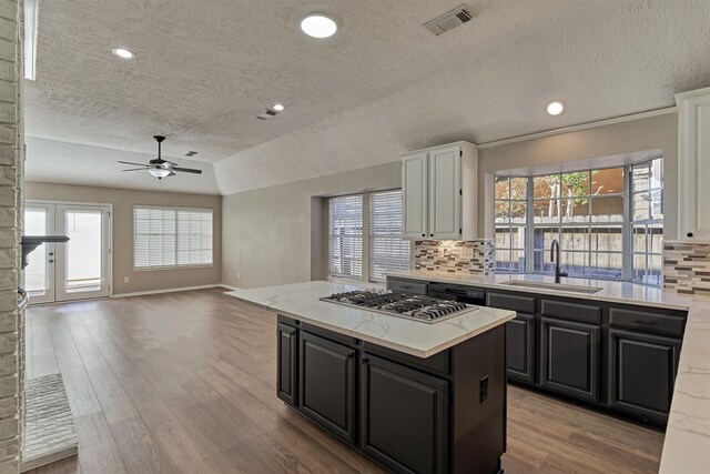 kitchen with sink, a center island, stainless steel gas cooktop, tasteful backsplash, and light wood-type flooring