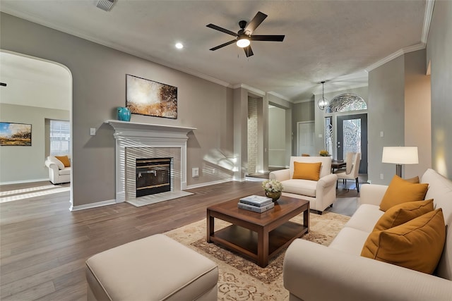 living room featuring a tiled fireplace, crown molding, light hardwood / wood-style flooring, and plenty of natural light