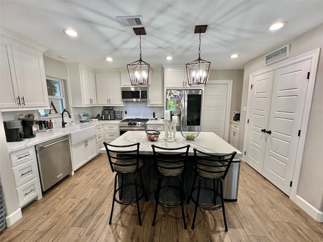 kitchen with light wood-type flooring, stainless steel appliances, white cabinetry, a kitchen island, and hanging light fixtures