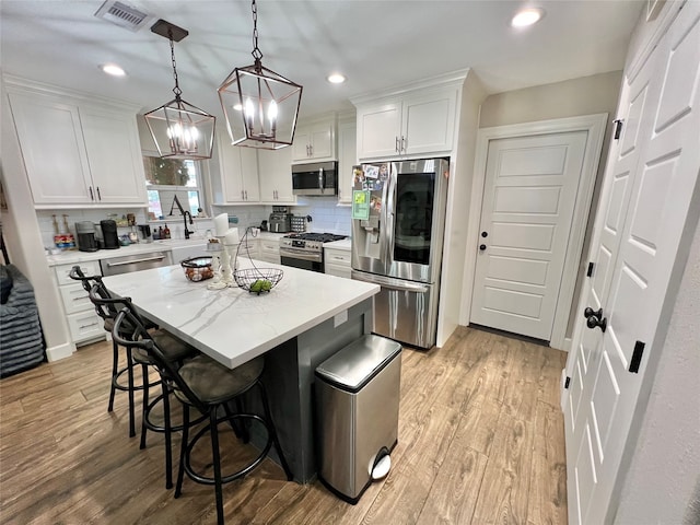 kitchen with white cabinets, a kitchen breakfast bar, light hardwood / wood-style floors, a kitchen island, and stainless steel appliances