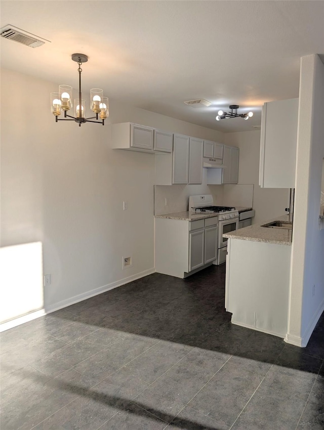 kitchen with dark tile patterned floors, an inviting chandelier, white cabinets, hanging light fixtures, and white gas stove