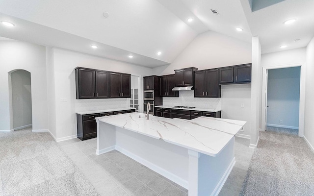 kitchen with arched walkways, stainless steel appliances, tasteful backsplash, and a large island with sink