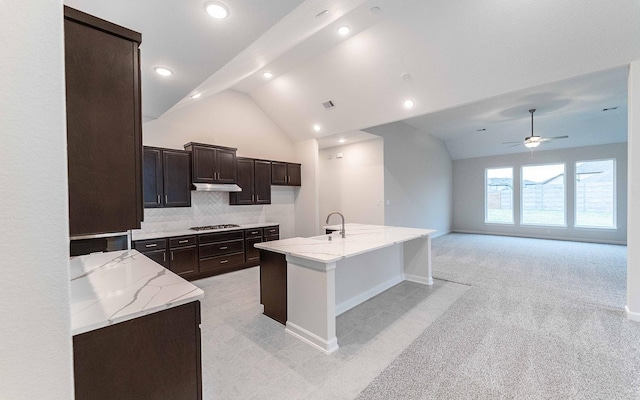 kitchen with under cabinet range hood, a sink, open floor plan, a center island with sink, and stainless steel gas stovetop