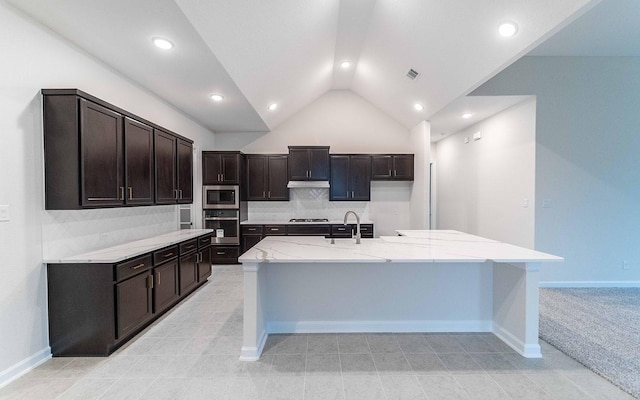 kitchen with a center island with sink, stainless steel appliances, a sink, dark brown cabinetry, and under cabinet range hood