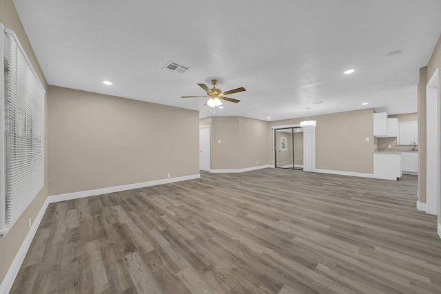 unfurnished living room featuring ceiling fan with notable chandelier, light hardwood / wood-style floors, and sink