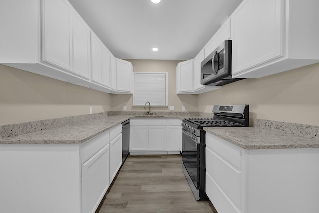 kitchen with light wood-type flooring, light stone counters, stainless steel appliances, sink, and white cabinetry