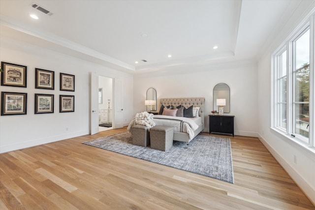 bedroom with a tray ceiling, ensuite bathroom, and light hardwood / wood-style floors