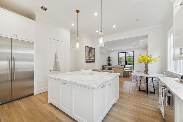 kitchen with light stone countertops, light wood-type flooring, stainless steel appliances, pendant lighting, and white cabinets