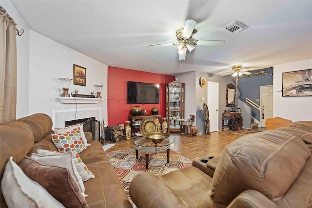 living room with ceiling fan, wood-type flooring, a fireplace, and a textured ceiling