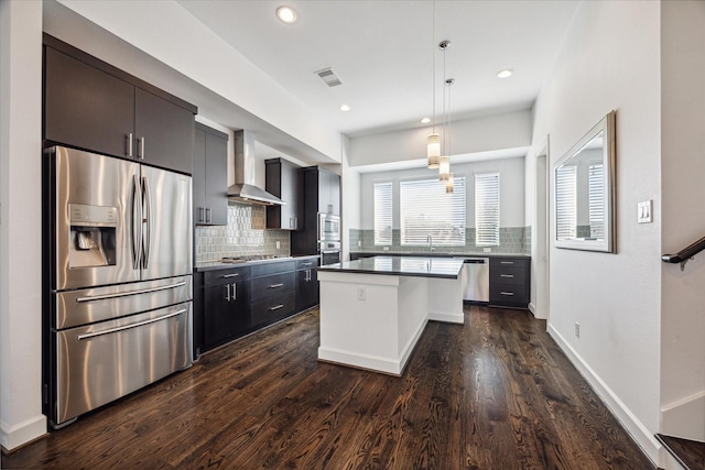 kitchen with decorative light fixtures, a kitchen breakfast bar, a center island, stainless steel appliances, and wall chimney exhaust hood