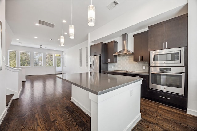 kitchen featuring ceiling fan, wall chimney range hood, dark hardwood / wood-style floors, a kitchen island, and appliances with stainless steel finishes