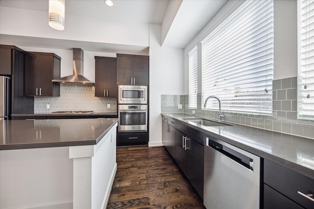 kitchen with stainless steel appliances, dark wood-type flooring, a sink, dark brown cabinets, and wall chimney range hood