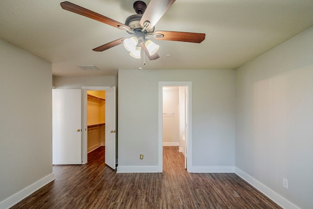 unfurnished bedroom with a closet, a walk in closet, dark hardwood / wood-style floors, and ceiling fan