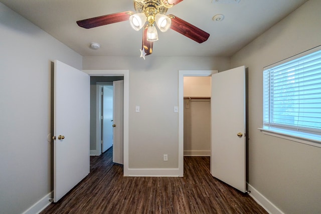 unfurnished bedroom with ceiling fan, a closet, a spacious closet, and dark hardwood / wood-style floors