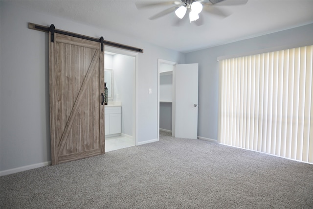 unfurnished bedroom with carpet flooring, ensuite bath, ceiling fan, a barn door, and a closet