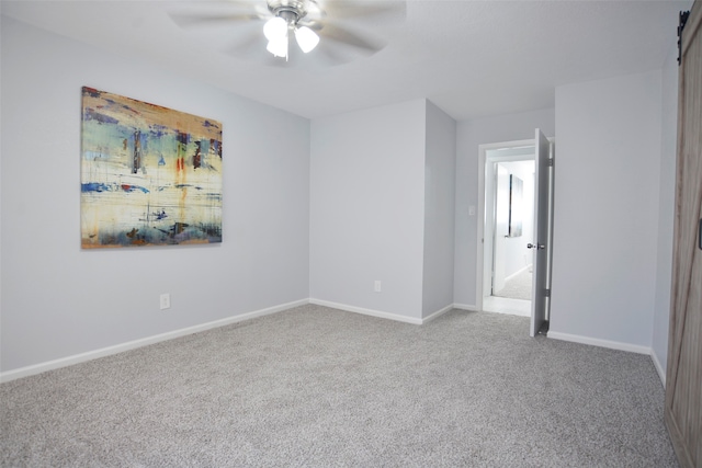 unfurnished bedroom featuring light carpet, a barn door, and ceiling fan