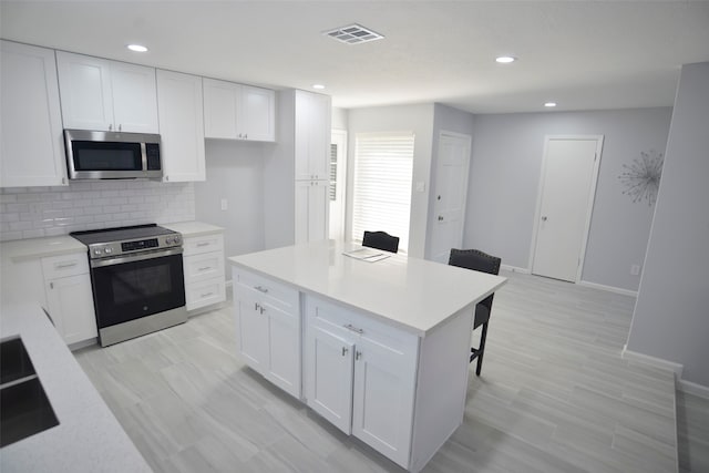 kitchen featuring a center island, backsplash, appliances with stainless steel finishes, a kitchen bar, and white cabinetry