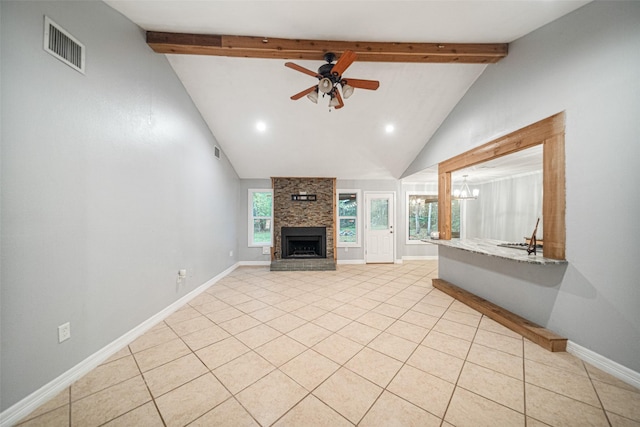 unfurnished living room with ceiling fan with notable chandelier, beam ceiling, a stone fireplace, and light tile patterned floors