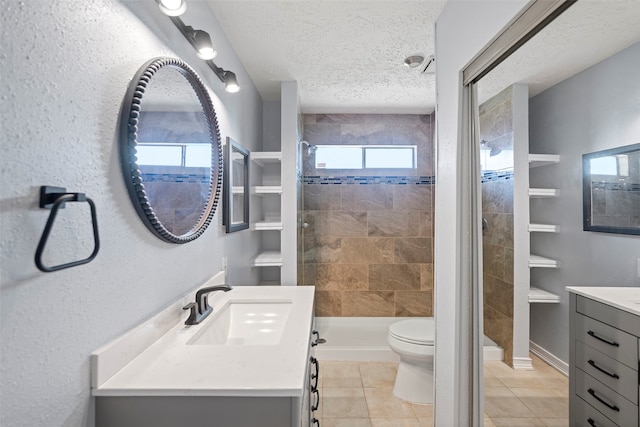 bathroom with a tile shower, vanity, a textured ceiling, tile patterned flooring, and toilet