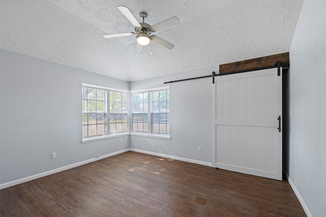 spare room featuring ceiling fan, a barn door, dark hardwood / wood-style flooring, and a textured ceiling