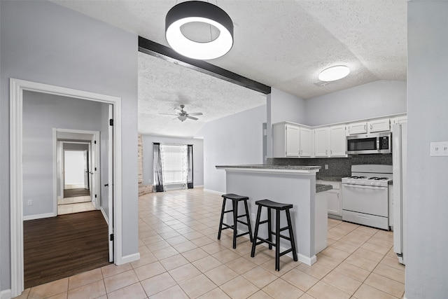 kitchen with vaulted ceiling with beams, kitchen peninsula, white appliances, a kitchen bar, and white cabinets