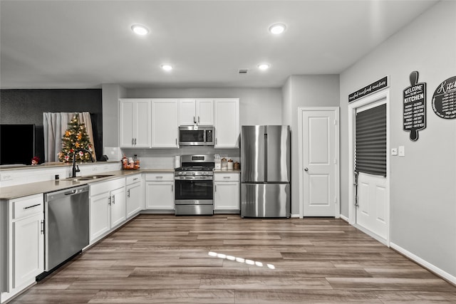 kitchen with kitchen peninsula, appliances with stainless steel finishes, sink, light hardwood / wood-style flooring, and white cabinetry