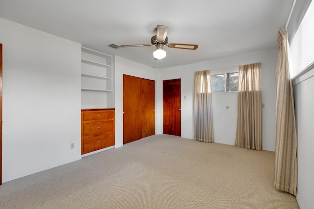 unfurnished bedroom with multiple closets, ceiling fan, and light colored carpet