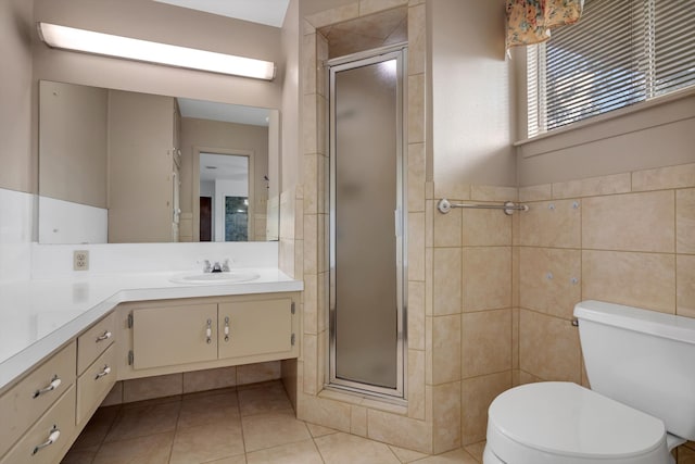 bathroom with tile patterned floors, toilet, a shower with door, vanity, and tile walls