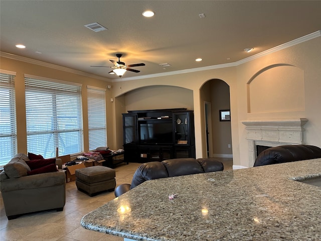 tiled living room featuring a textured ceiling, ceiling fan, crown molding, and a tiled fireplace