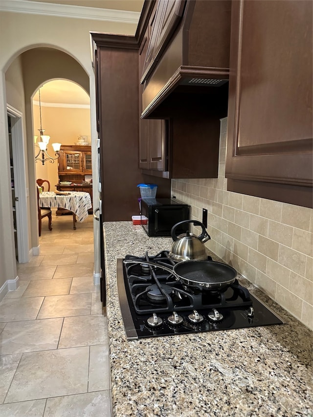 kitchen featuring backsplash, premium range hood, black stovetop, light stone countertops, and dark brown cabinets