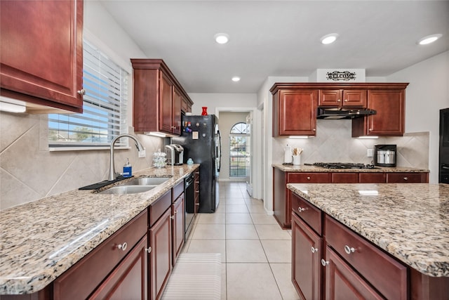 kitchen with light stone countertops, black appliances, decorative backsplash, sink, and light tile patterned floors