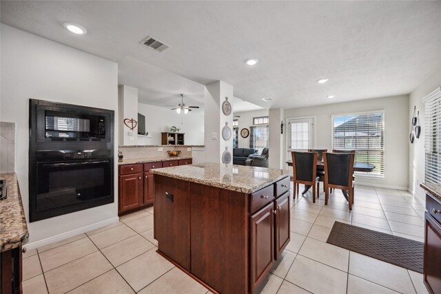 kitchen featuring light tile patterned floors, ceiling fan, light stone countertops, black appliances, and a center island