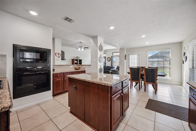 kitchen with ceiling fan, a kitchen island, light stone countertops, black appliances, and light tile patterned flooring