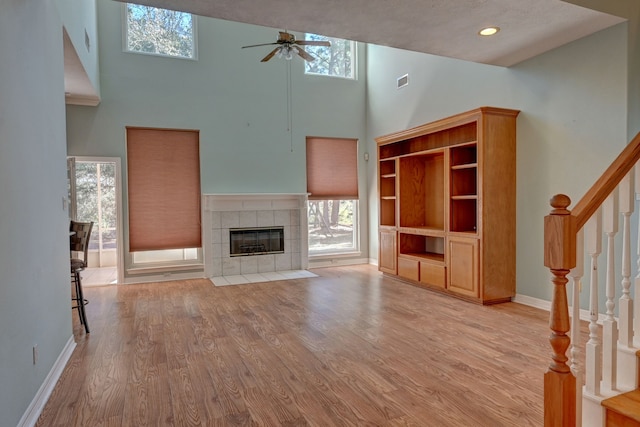 unfurnished living room featuring light wood-type flooring, a towering ceiling, a textured ceiling, ceiling fan, and a fireplace