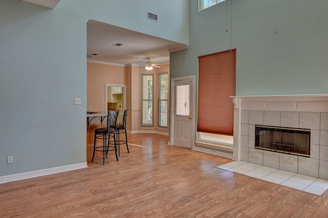 living room with a towering ceiling, ceiling fan, crown molding, a tile fireplace, and light hardwood / wood-style flooring