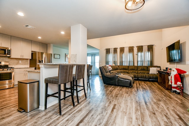 kitchen with light stone counters, light hardwood / wood-style flooring, a kitchen bar, white cabinets, and appliances with stainless steel finishes