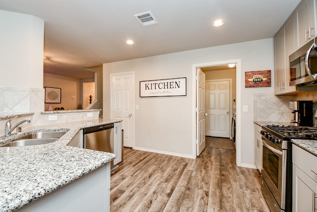 kitchen featuring light stone countertops, sink, light hardwood / wood-style floors, decorative backsplash, and appliances with stainless steel finishes