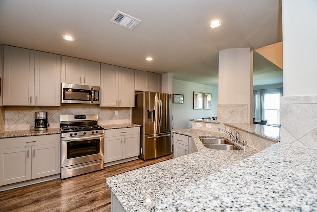 kitchen featuring white cabinets, sink, appliances with stainless steel finishes, light stone counters, and kitchen peninsula