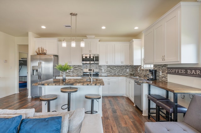 kitchen featuring dark wood-type flooring, white cabinets, an island with sink, decorative light fixtures, and stainless steel appliances