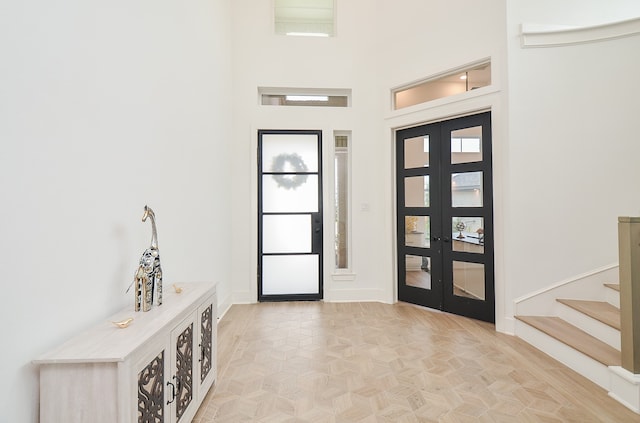 foyer with light parquet floors, a towering ceiling, and french doors