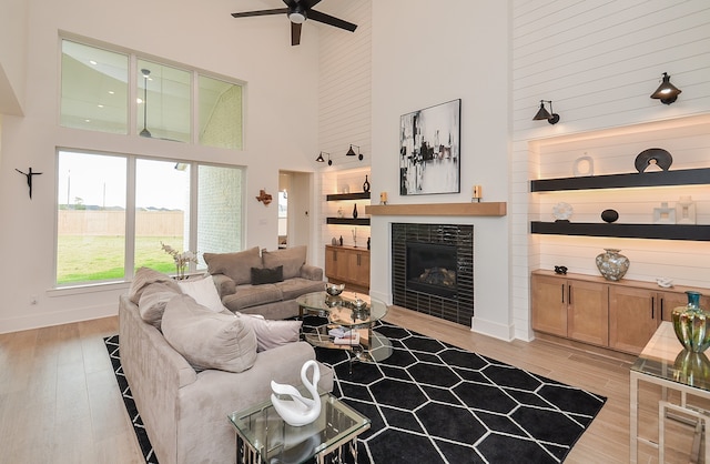 living room featuring a fireplace, ceiling fan, light hardwood / wood-style flooring, and a high ceiling