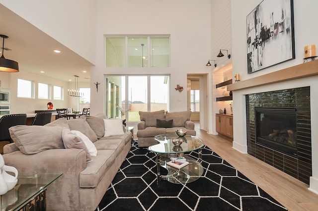 living room with light hardwood / wood-style floors, a towering ceiling, a healthy amount of sunlight, and a tiled fireplace