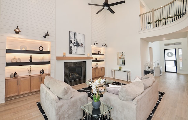 living room featuring a tile fireplace, ceiling fan, a towering ceiling, and light hardwood / wood-style floors