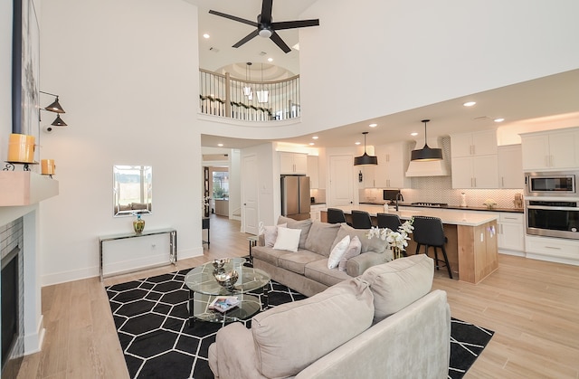 living room with ceiling fan, light hardwood / wood-style flooring, a high ceiling, and a brick fireplace