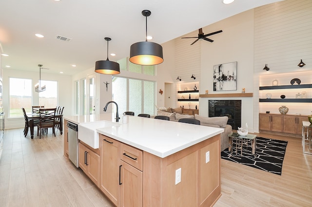 kitchen featuring sink, light brown cabinets, pendant lighting, a center island with sink, and a high ceiling