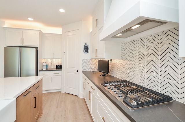 kitchen featuring white cabinetry, stainless steel appliances, tasteful backsplash, light hardwood / wood-style floors, and custom range hood